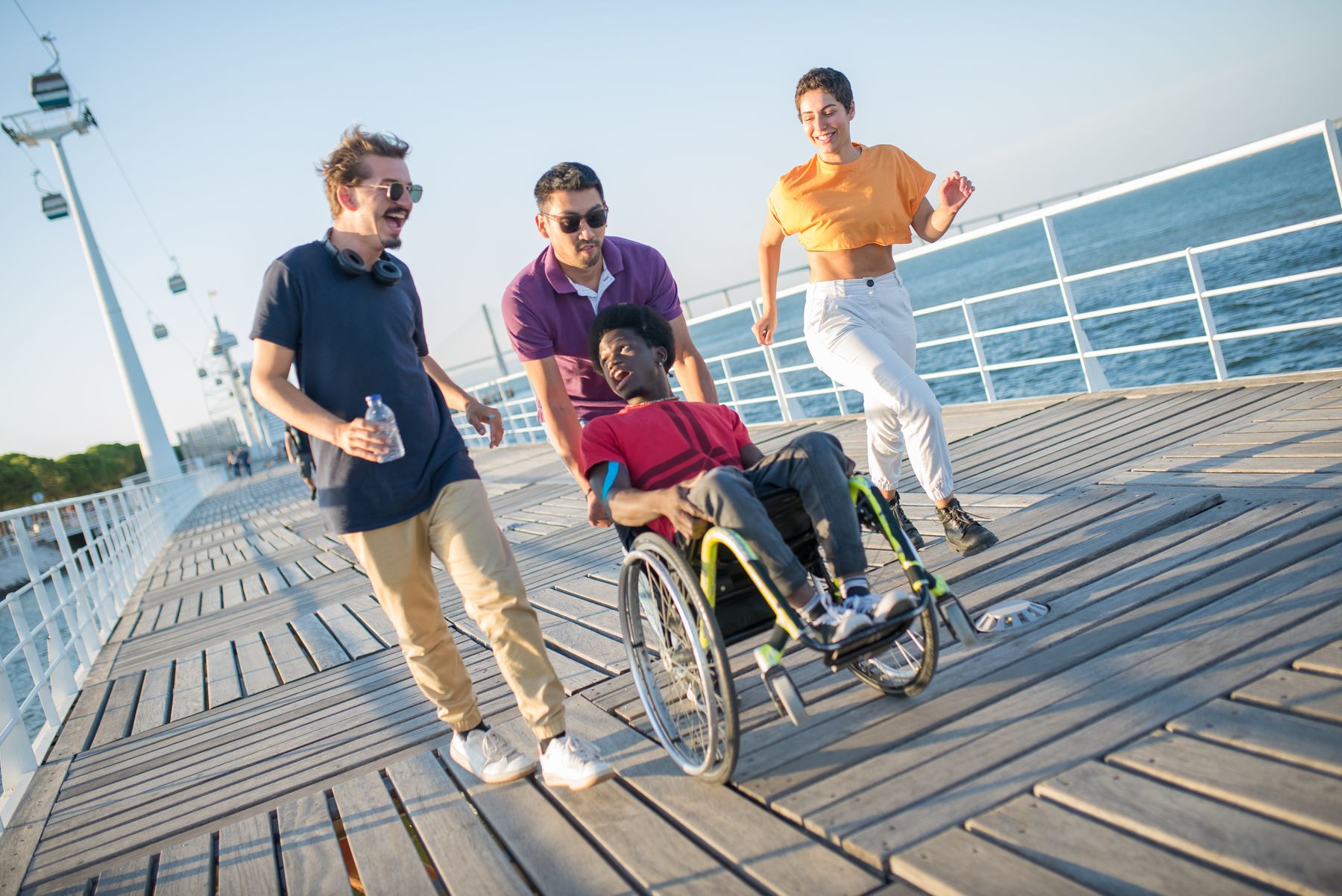 Four friends, including a wheelchair user, enjoying time together on a sunny boardwalk